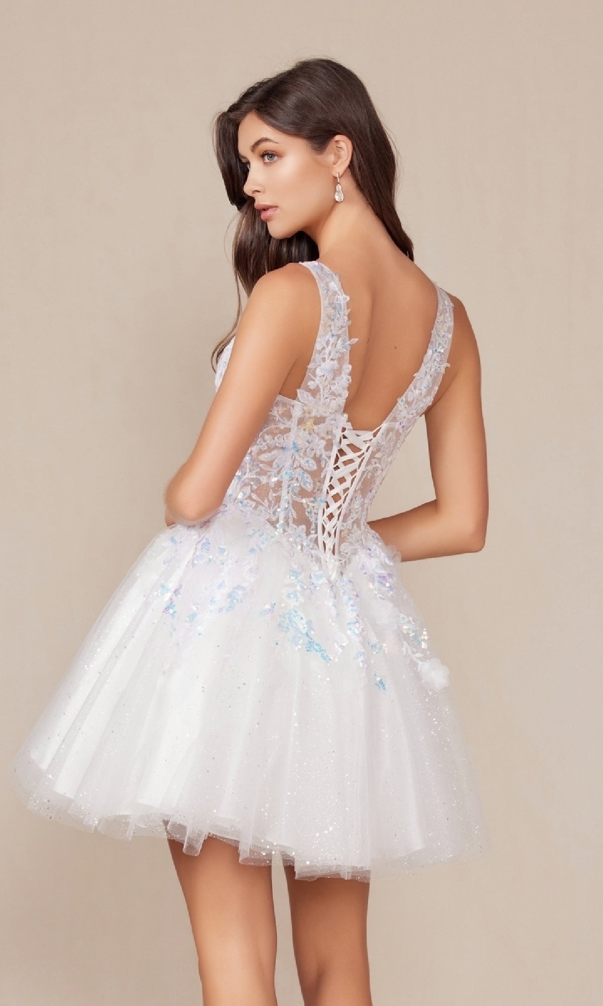 A woman models the Short White Glitter A-Line Homecoming Dress H846W, featuring a lace-up back, floral details, and a tulle skirt, against a neutral background.